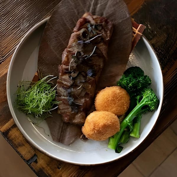 Asian-fusion dish with sliced meat, two fried croquettes, broccoli, and microgreens on a white plate.