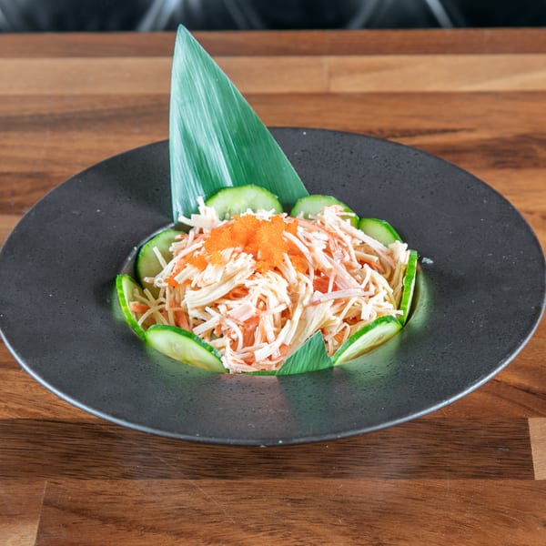 Ganzo Sushi's crab salad with cucumber slices and orange tobiko on a dark plate.