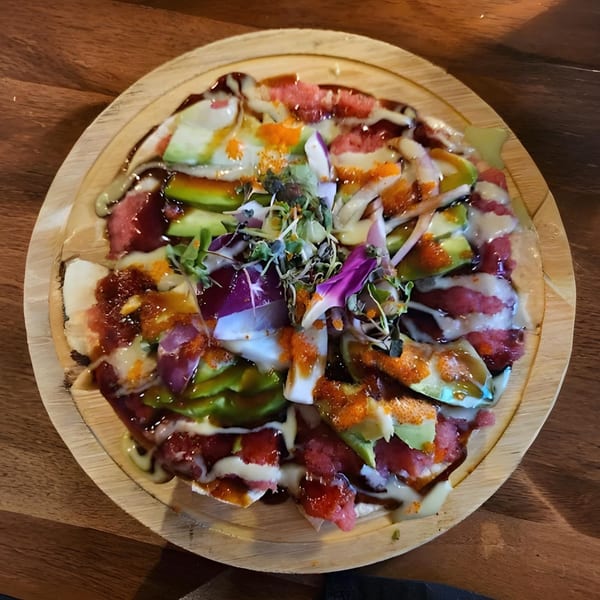 Ganzo Sushi's Asian-fusion pizza with tuna, avocado, roe, and microgreens on a wooden plate.